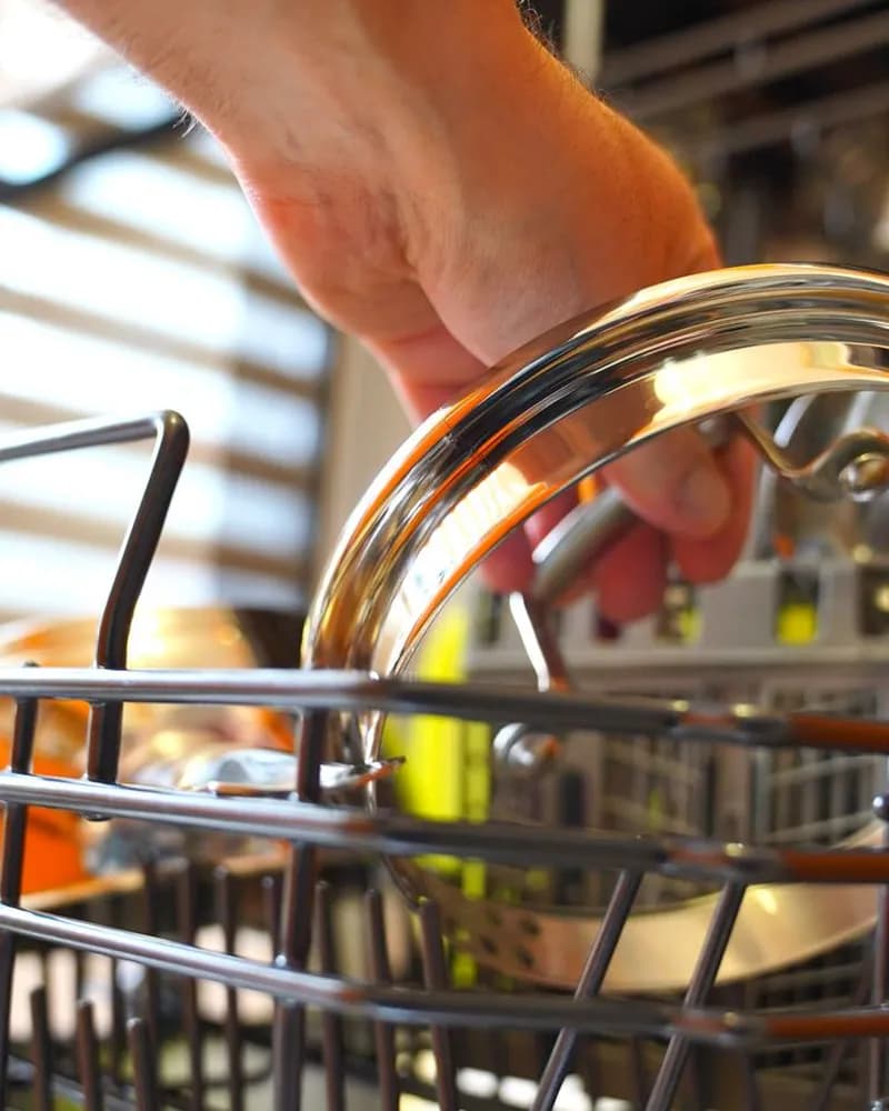 Hands loading a glass bowl into a dishwasher rack