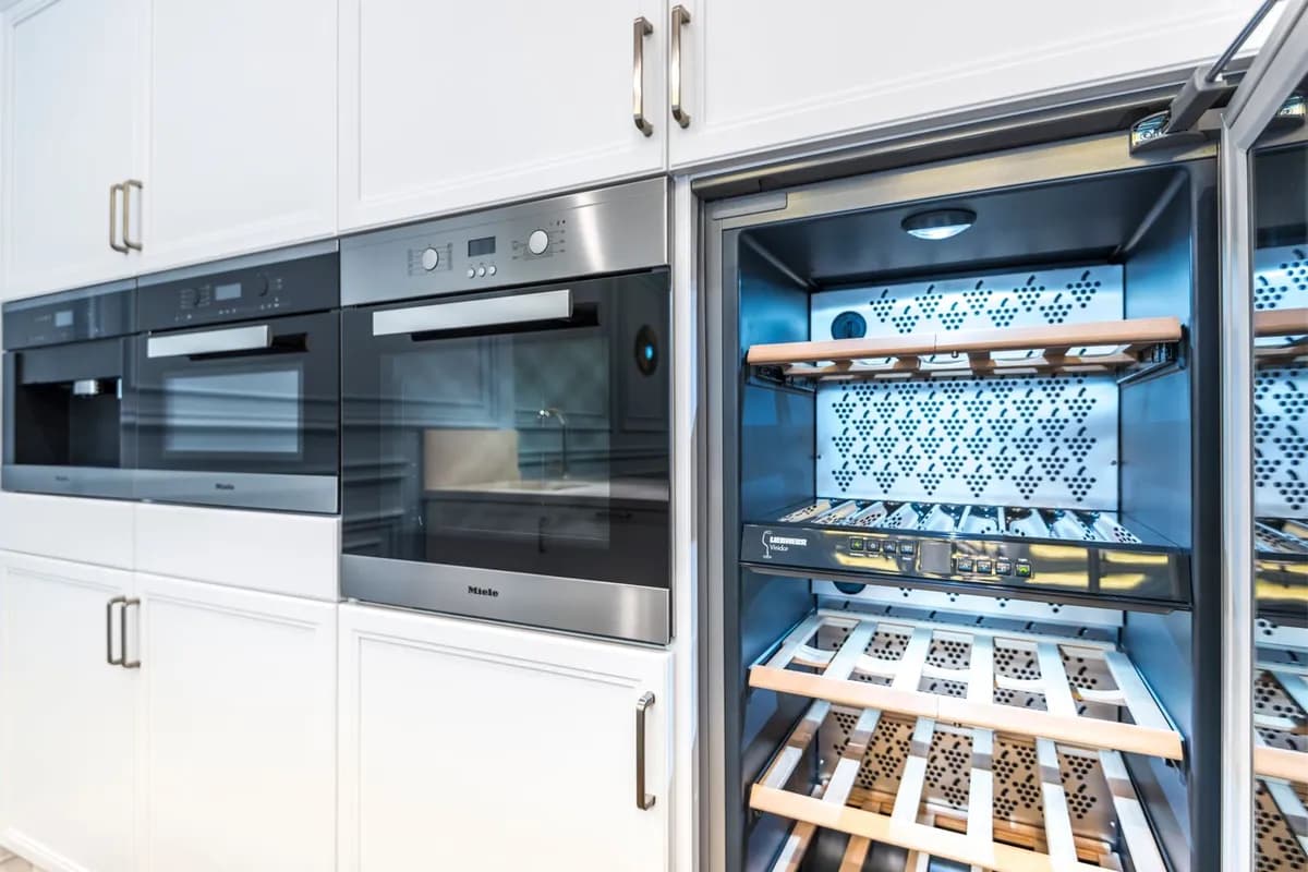 Built-in wine cooler with its door open beside built-in ovens
